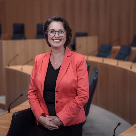 Die Vizepräsidentin des Landtags Rheinland-Pfalz, Kathrin Anklam-Trapp. Das Foto ist horizontal ausgerichtet. Die Vizepräsidentin steht lächelnd zwischen den Stuhlreihen des Plenarsaals.