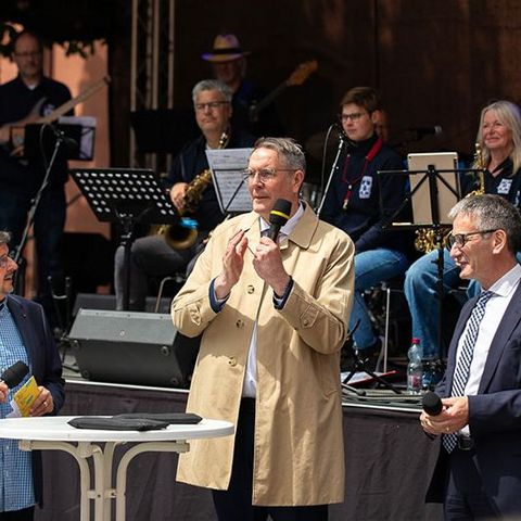 Der Ministerpräsident spricht in ein Mikrofon. Der Landtagspräsident und der Leiter der Blue Light Big Band des Polizeipräsidiums Ludwigshafen stehen neben ihm.