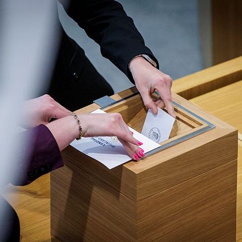 Zwei Hände werfen Stimmzettel in eine Wahlurne.