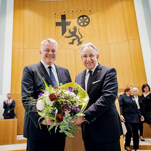 Gordon Schnieder und Matthias Lammert stehen nebeneinander im Plenarsaal und halten gemeinsam einen großen Blumenstrauß. Im Hintergrund applaudieren mehrere Personen.