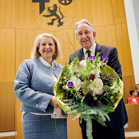 Marion Schneid und Matthias Lammert stehen nebeneinander im Plenarsaal und halten gemeinsam einen großen Blumenstrauß. Im Hintergrund sitzen mehrere Personen.