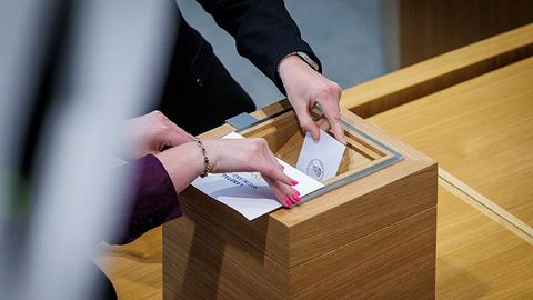 Zwei Hände werfen Stimmzettel in eine Wahlurne.