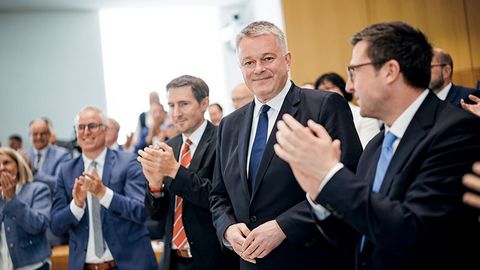 Ministerpräsident Gordon Schnieder steht inmitten applaudierender Abgeordneter.