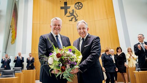 Gordon Schnieder und Matthias Lammert stehen nebeneinander im Plenarsaal und halten gemeinsam einen großen Blumenstrauß. Im Hintergrund applaudieren mehrere Personen.
