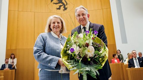Marion Schneid und Matthias Lammert stehen nebeneinander im Plenarsaal und halten gemeinsam einen großen Blumenstrauß. Im Hintergrund sitzen mehrere Personen.
