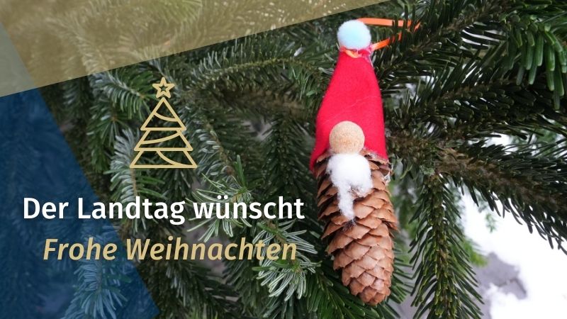 Symbolbild Weihnachten: Tannenzweige mit weihnachtlich dekoriertem Tannenzapfen und einem Text: Der Landtag wünscht frohe Weihnachten 