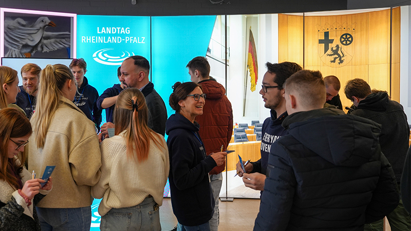 Mehrere Personen im Gespräch miteinander; stehend vor dem Hintergrund des Plenarsaals für das Projekt "Landtag goes Berufsschule"