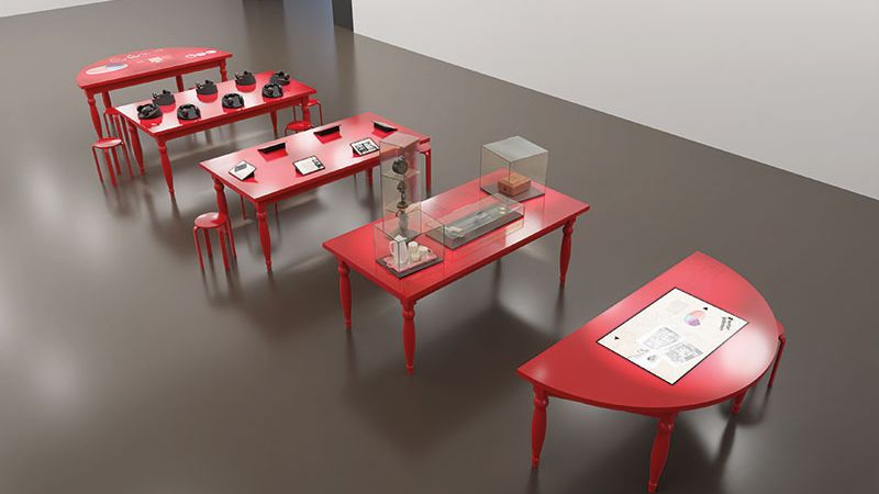 Die Ausstellungsstücke der Wanderausstellung liegen auf roten Tischen aus. Das Bild ist aus der Vogelperspektive aufgenommen.