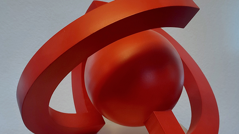 Rote abstrakte Skulptur mit einer gro&szlig;en Kugel, die von einem langen mehrfach gebogenen Element umgeben ist