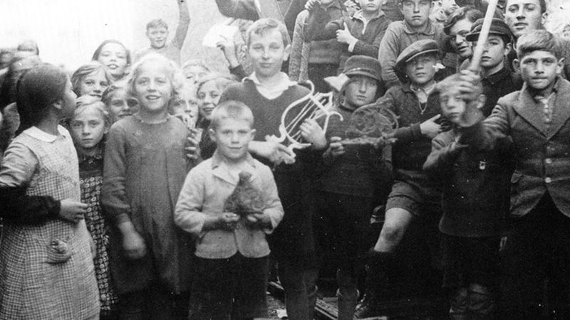 Das schwarz-weiß Foto zeigt zahlreiche Kinder, die verschiedene Gegenstände in den Händen halten.