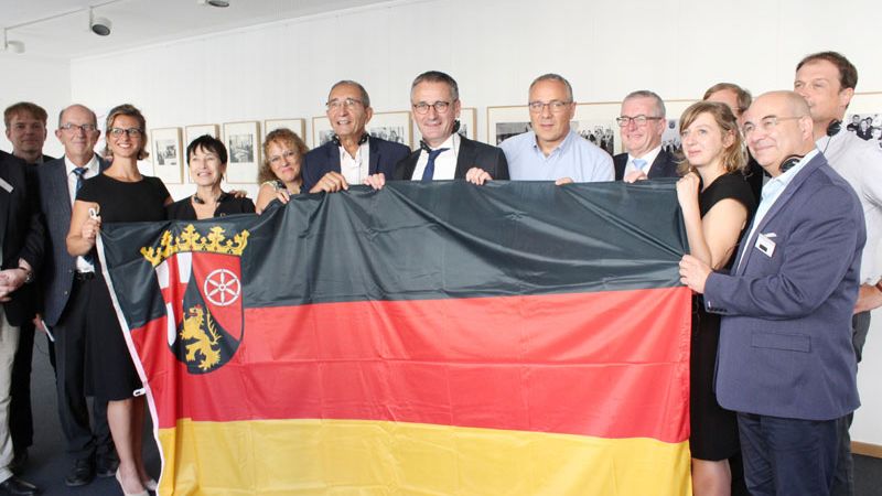 Eine Delegation aus der Partnerregion Burgund-Franche-Comté im Haus Burgund in Mainz; die Teilnehmer halten die rheinland-pfälzische Flagge.