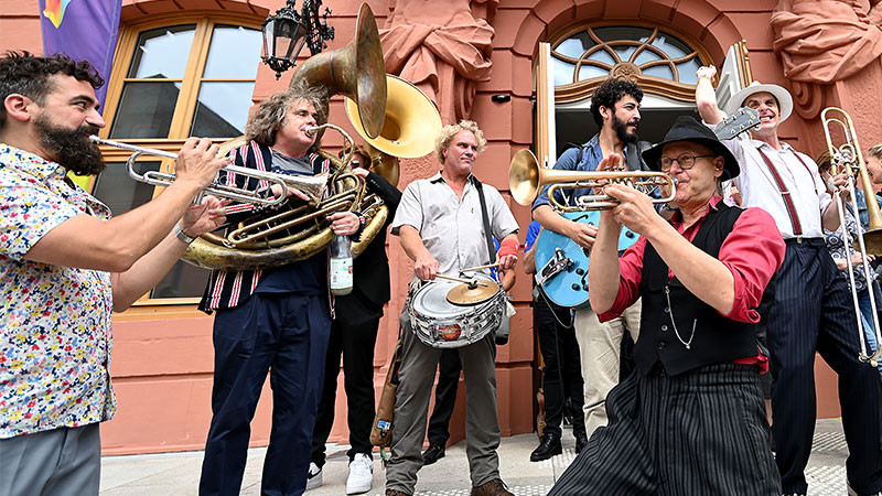Musiker mit unterschiedlichen Musikinstrumenten spielen vor dem Haupteingang des Landtags RLP.