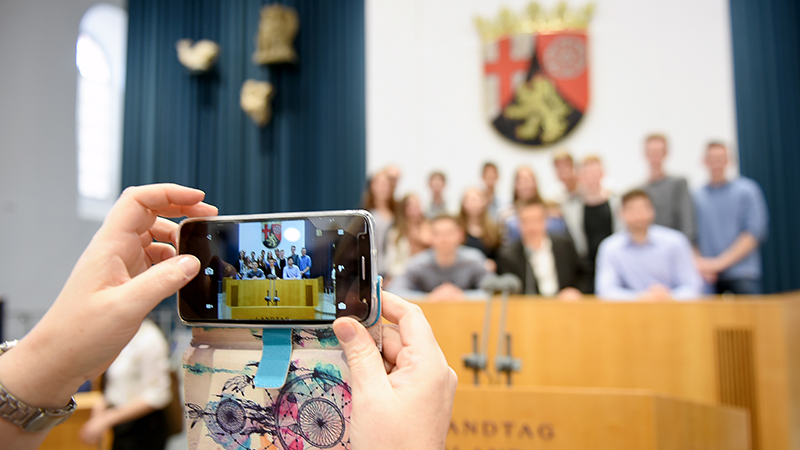 Ausschnitt aus der Veranstaltung Jugend debattiert von 2017. Ein Smartphone im Fokus, beim Fotografieren der Gruppe.