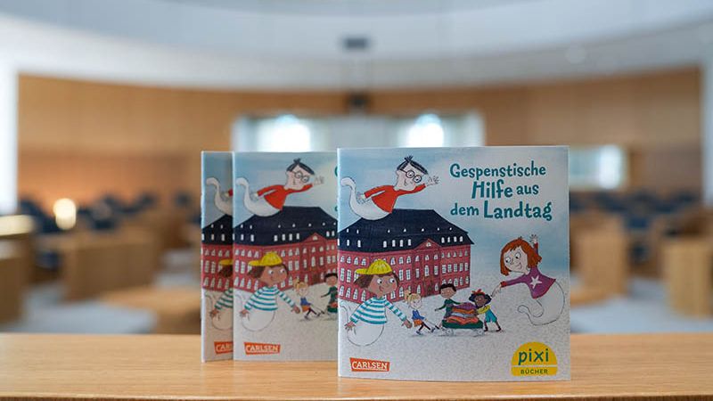 Zu sehen sind drei Pixi-Bücher mit dem Titel: "Gespenstische Hilfe aus dem Landtag". Im Hintergrund sieht man den Plenarsaal.