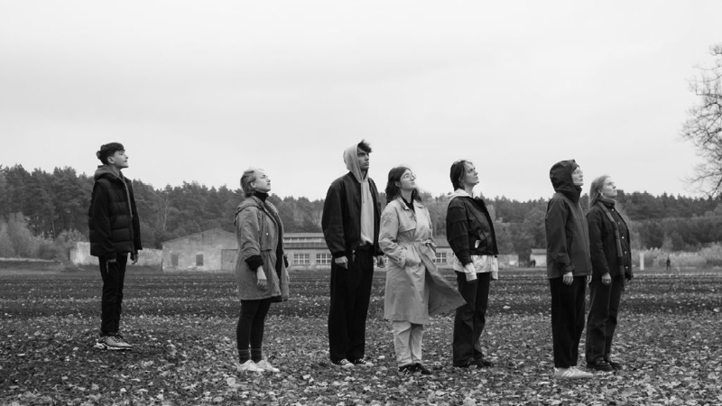Auf dem schwarz-weiß Foto sieht man sieben Jugendliche. Sie stehen auf einem großen Feld. Alle Personen schauen in die rechte Hälfte des Bildes.