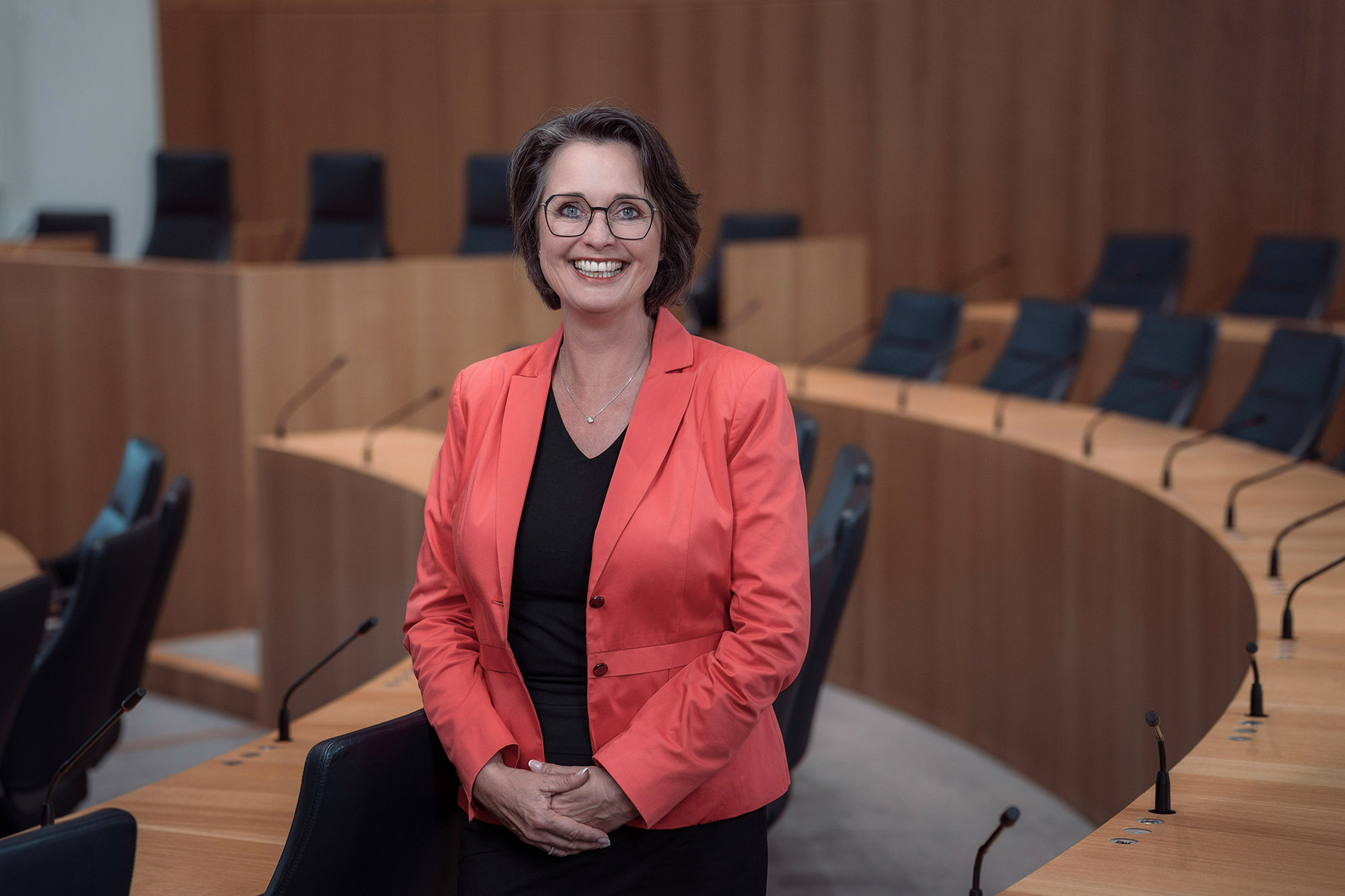 Die Vizepräsidentin des Landtags Rheinland-Pfalz, Kathrin Anklam-Trapp. Das Foto ist horizontal ausgerichtet. Die Vizepräsidentin steht lächelnd zwischen den Stuhlreihen des Plenarsaals.