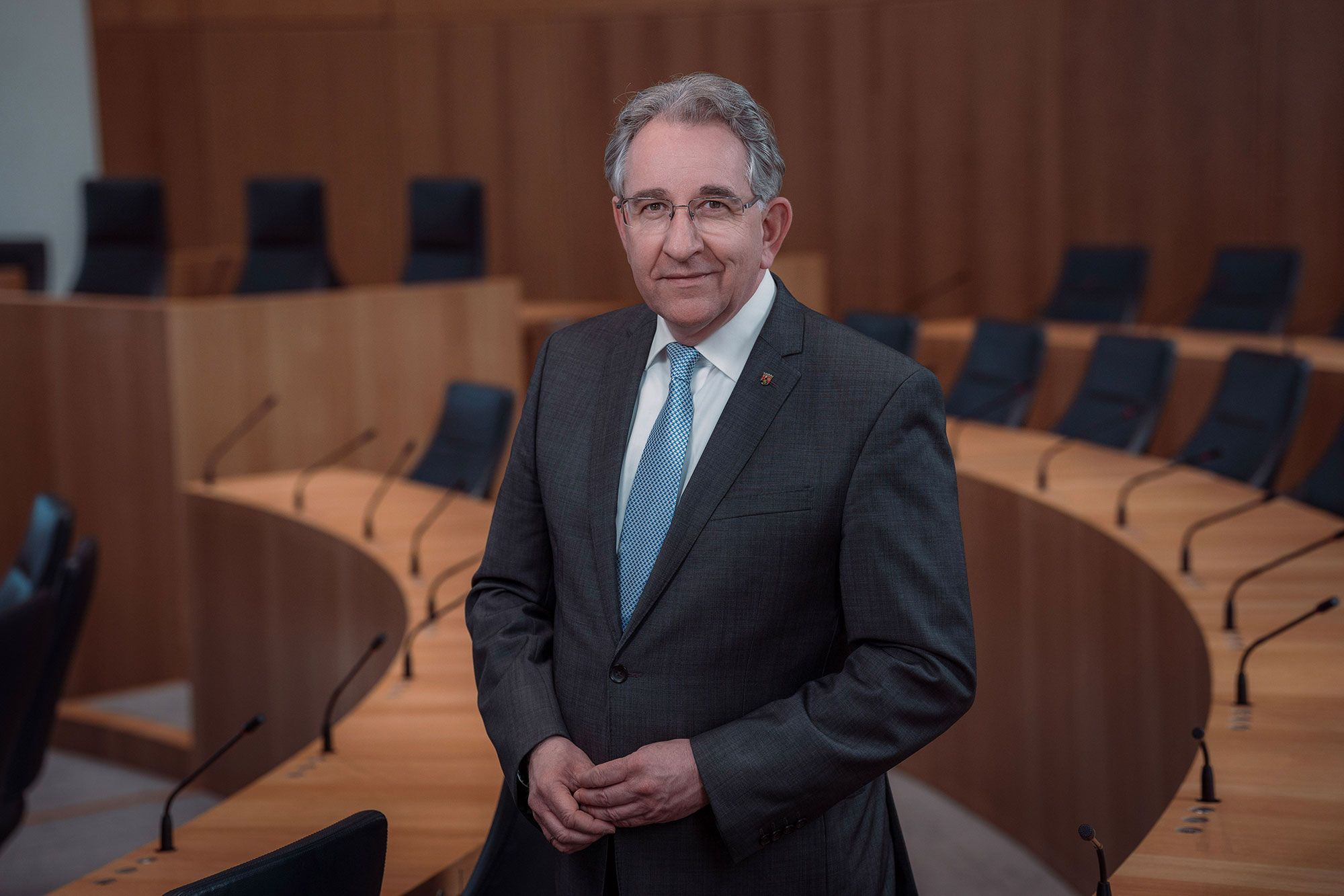 Der Vizepräsident des Landtags Rheinland-Pfalz, Matthias Lammert. Das Foto ist horizontal ausgerichtet. Der Vizepräsident steht lächelnd zwischen den Stuhlreihen des Plenarsaals.