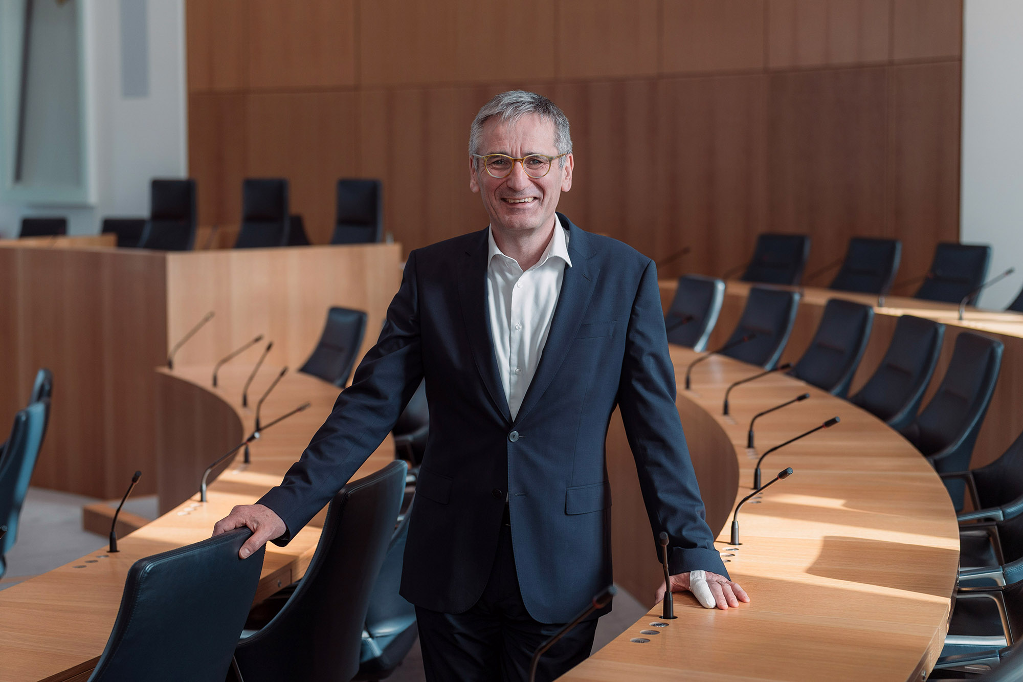 Landtagspräsident  Hendrik Hering im Plenarsaal des Deutschhauses; der Präsident steht zwischen zwei Sitzreihen; er lächelt, die Stimmung ist locker; im Hintergrund ist das Rednerpult zu sehen