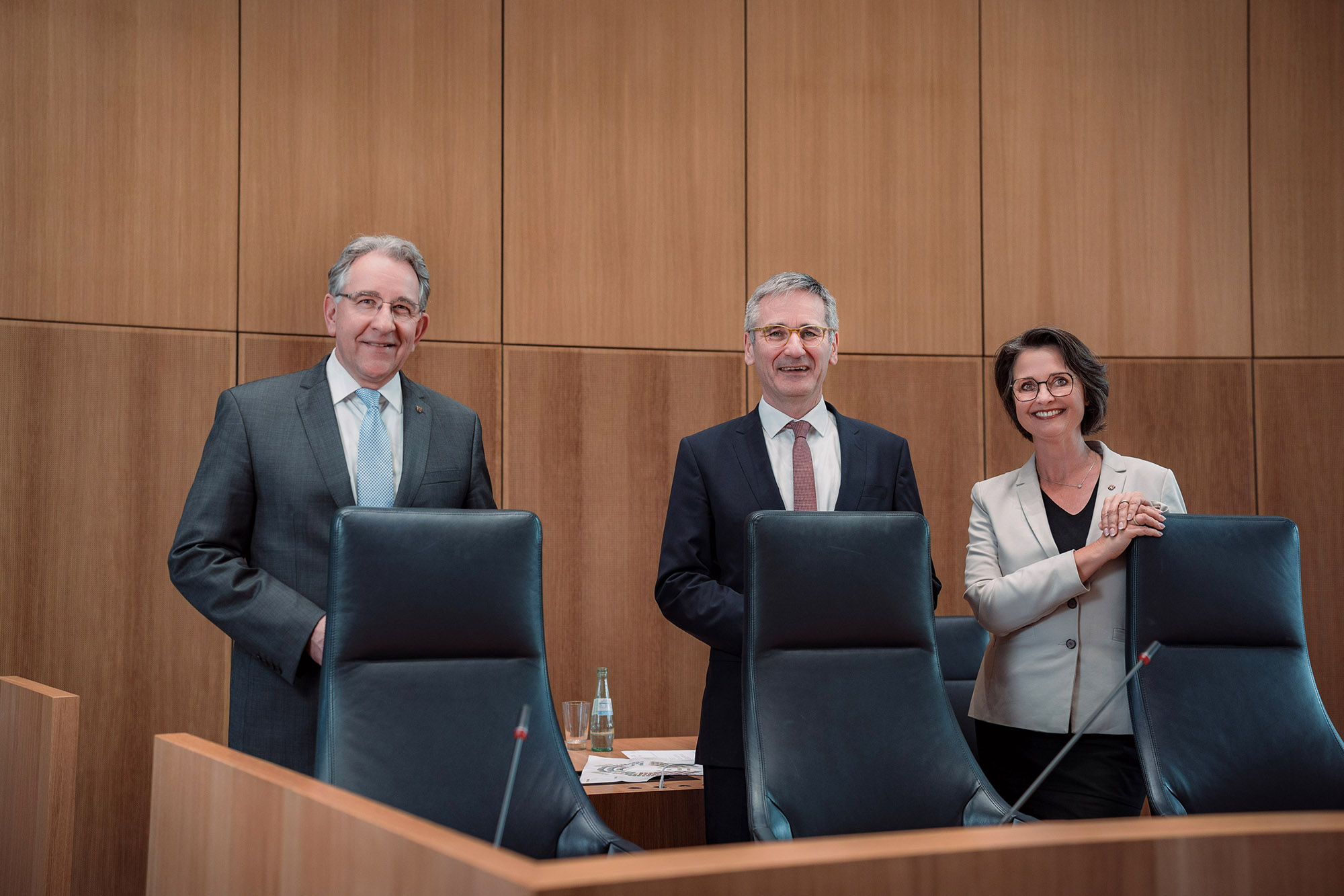 Die Mitglieder des Vorstands stehen lachend hinter den Sitzen des Sitzungsvorstands im Plenarsaal des Deutschhauses.