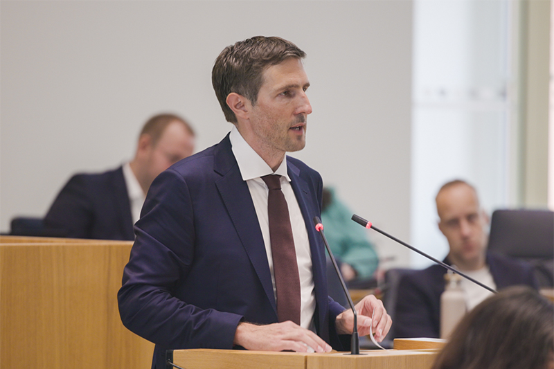 Ein Mann steht am Redepult im Plenarsaal und spricht in zwei Mikrofone.