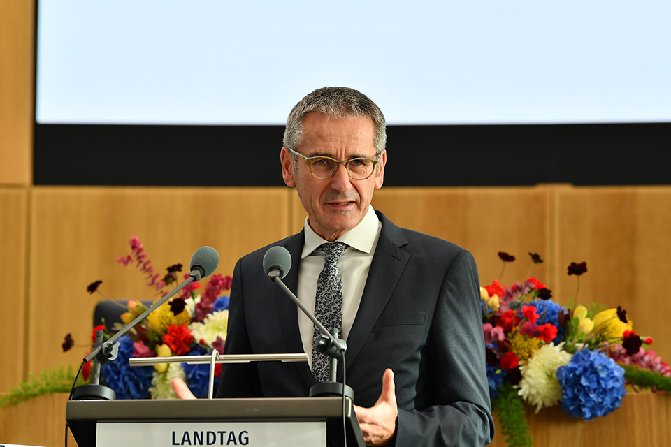 Hendrik Hering steht am Rednerpult im Plenarsaal. Im Hintergrund schmücken festliche Blumenbouquets den Tisch.