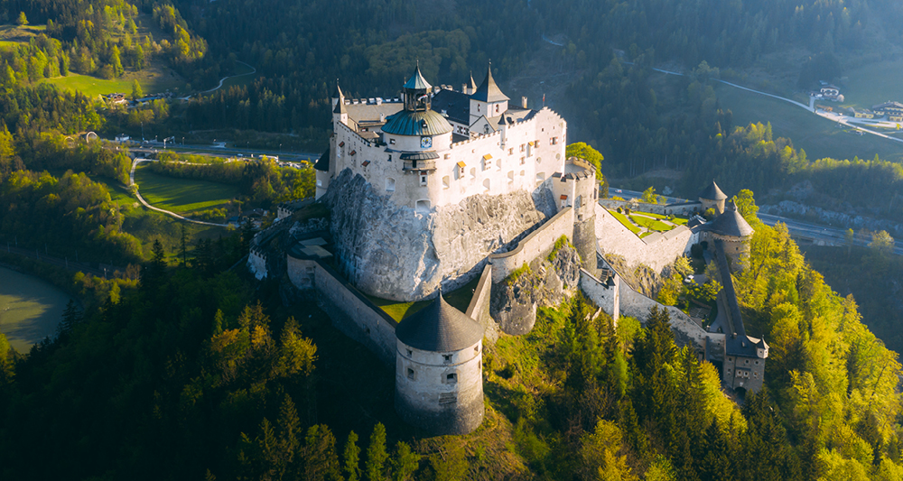 Zu sehen ist eine große mittelalterliche Burganlage, die auf einem Felsen über einer bewaldeten Landschaft thront. Die Burg hat dicke Mauern und Türme. Diese Anlage ist die Festung Hohenwerfen.