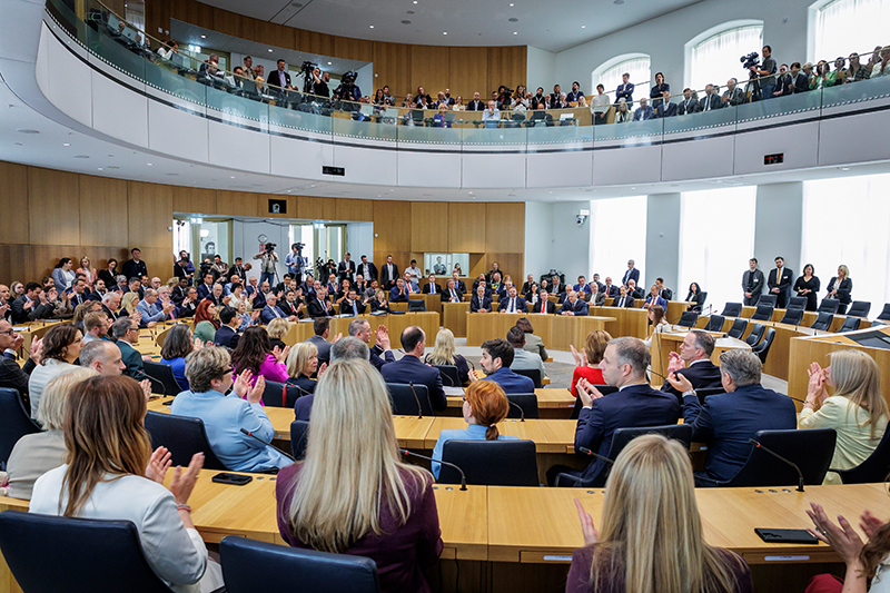 Die Abgeordneten sitzen applaudierend im Plenarsaal. Von der Besuchertribüne aus sehen zahlreiche Personen zu.