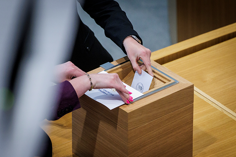Zwei Hände werfen Stimmzettel in eine Wahlurne.
