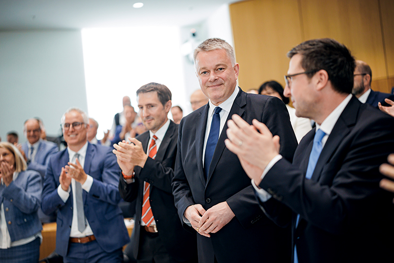 Ministerpräsident Gordon Schnieder steht inmitten applaudierender Abgeordneter.