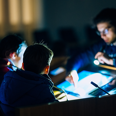 Zu sehen ist das Pult des Präsidenten im Plenarsaal im Dunkeln. Vor dem beleuchteten Pult stehen drei Kinder.