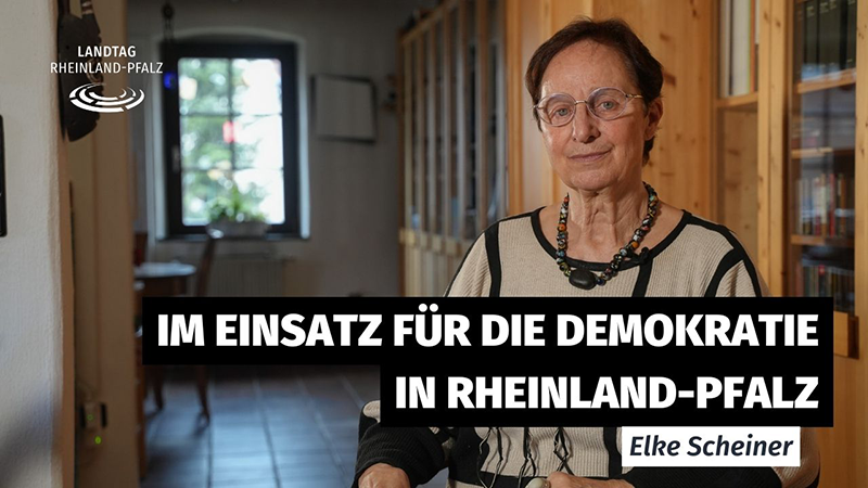 Eine Frau sitzend, im Hintergrund eine Wohnung mit Holzschränken. 