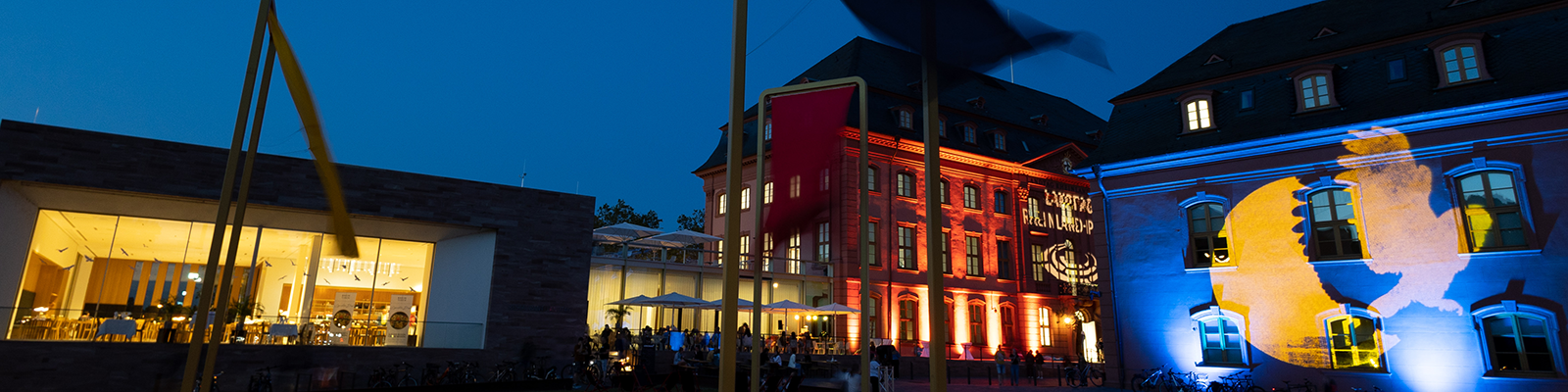 Zu sehen sind mehrere Gebäude die angeleuchtet werden, auf der rechten Seite sieht man das blau-gelbe Logo der Museumsnacht.