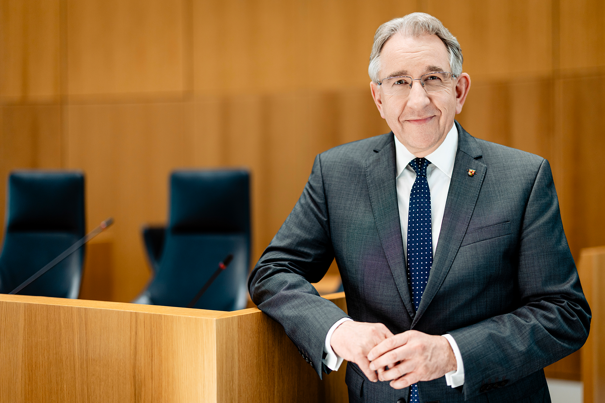 Zu sehen ist ein Mann stehend im leeren Plenarsaal.